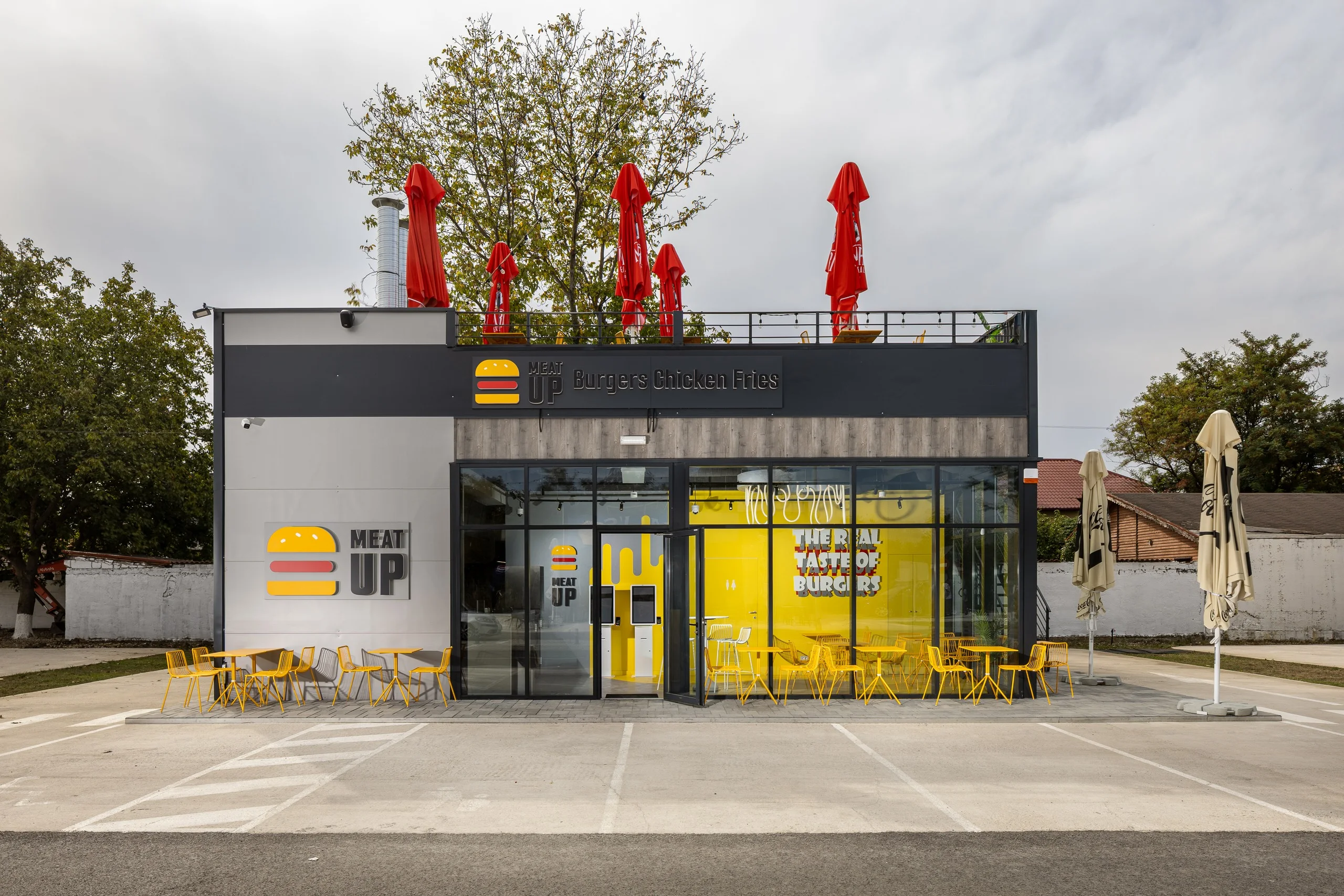 MeatUp - clădirea restaurantului, cu fațada vitrată și terasa cu umbrele roșii