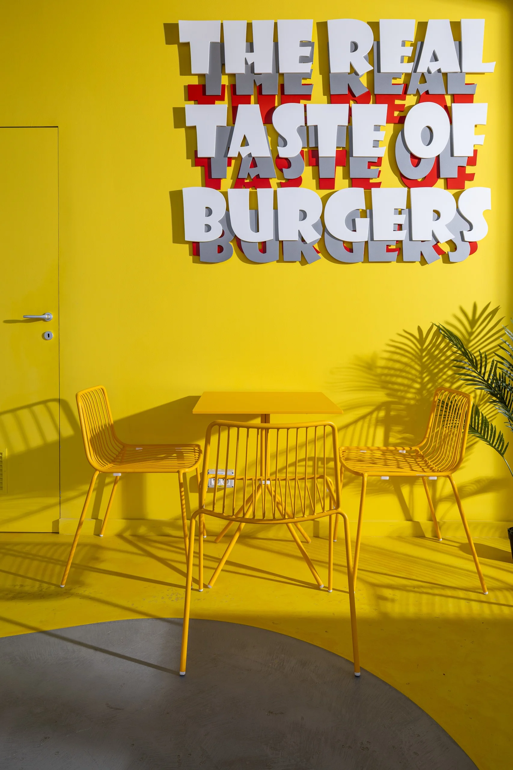 MeatUp - masă cu scaune galbene din sârmă sub mesajul „The real taste of burgers”